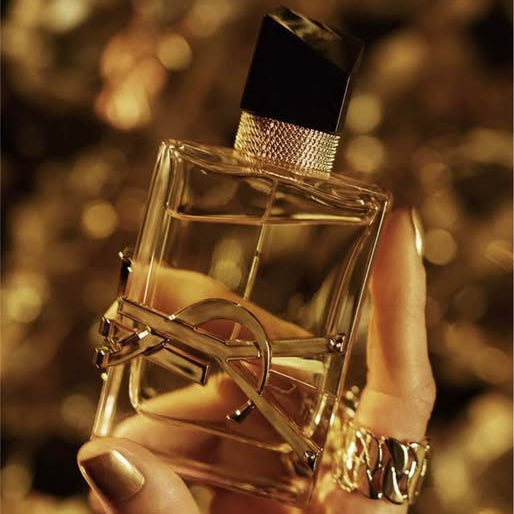 Gold perfume bottle held by a hand with a blurred golden background