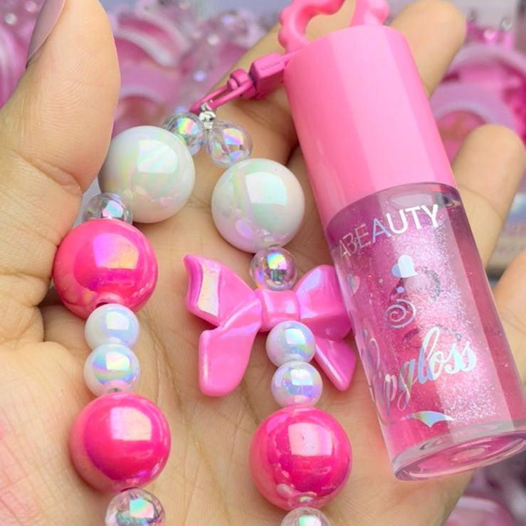 Hand holding a small pink beauty product with a beaded necklace featuring pink bows and white hearts.