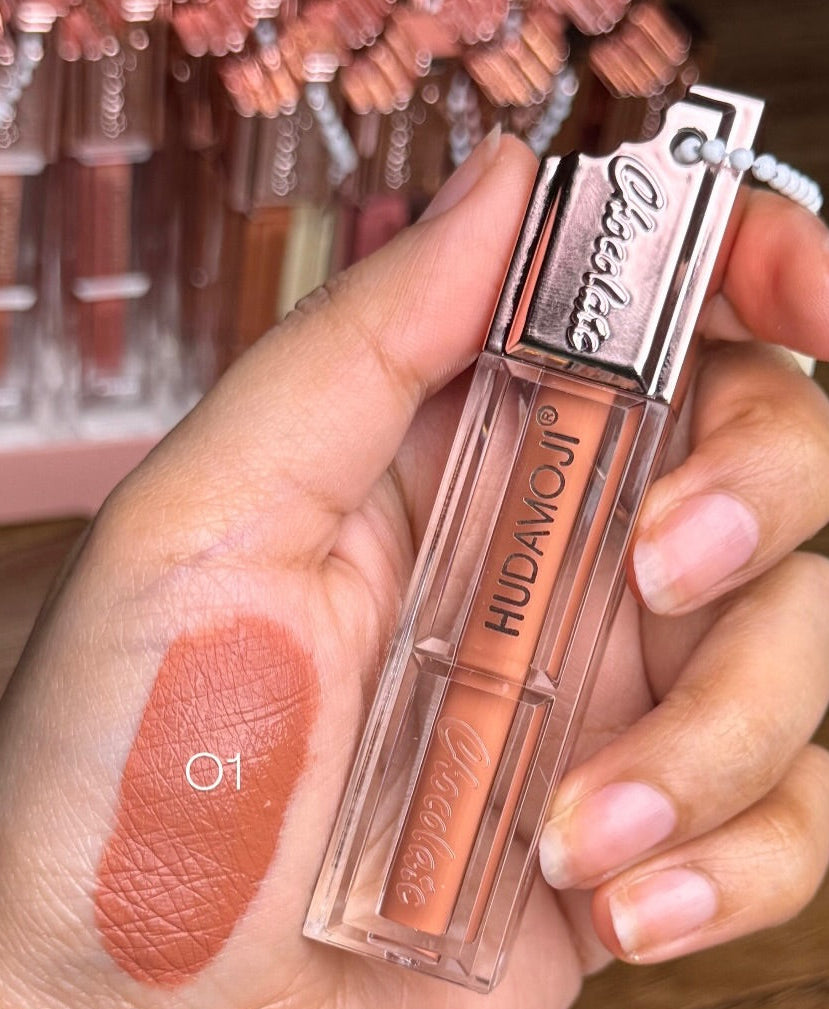 Hud avocado lip gloss held in hand with swatch on skin, blurred product display in background