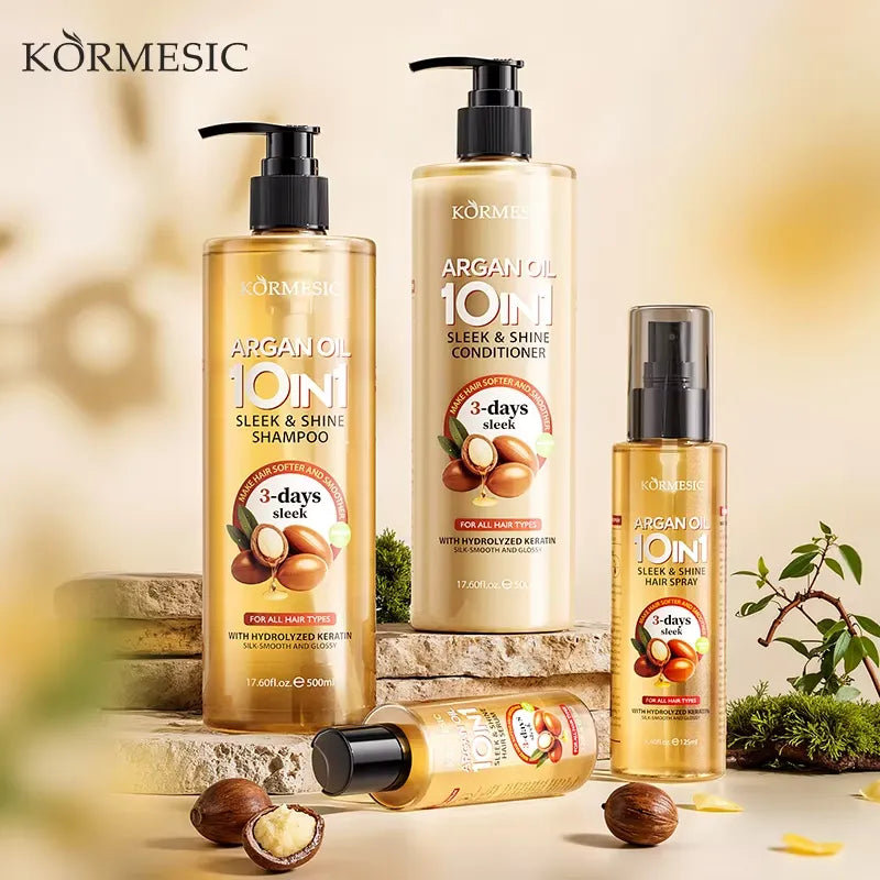 Four Körmesic hair care products arranged on stone blocks with whole and halved argan nuts and small greenery props against a warm beige background. The set includes shampoo, conditioner, a small spray bottle, and a tube, all in transparent bottles with golden liquid and black pumps/caps.