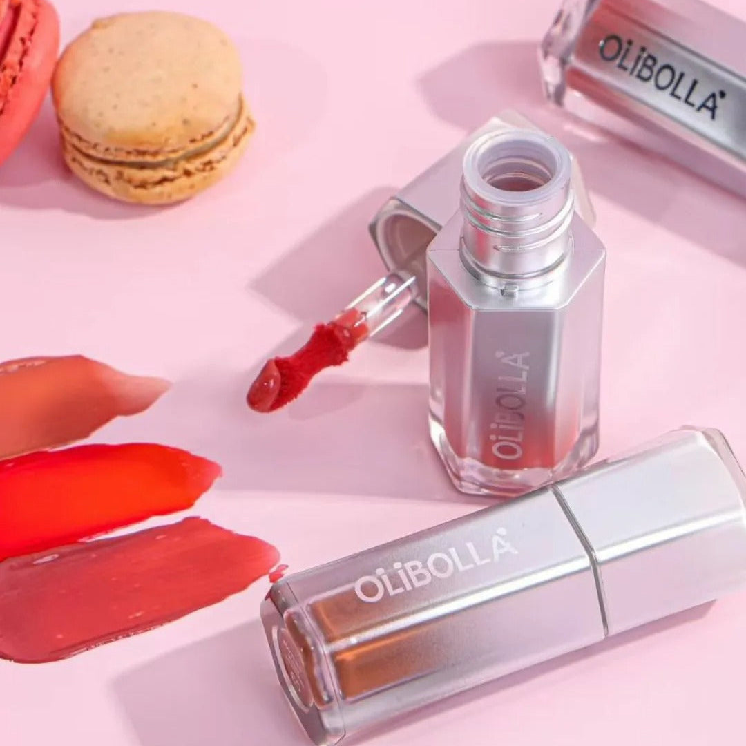 Olibella lip gloss and nail polish on a pink background with macarons.