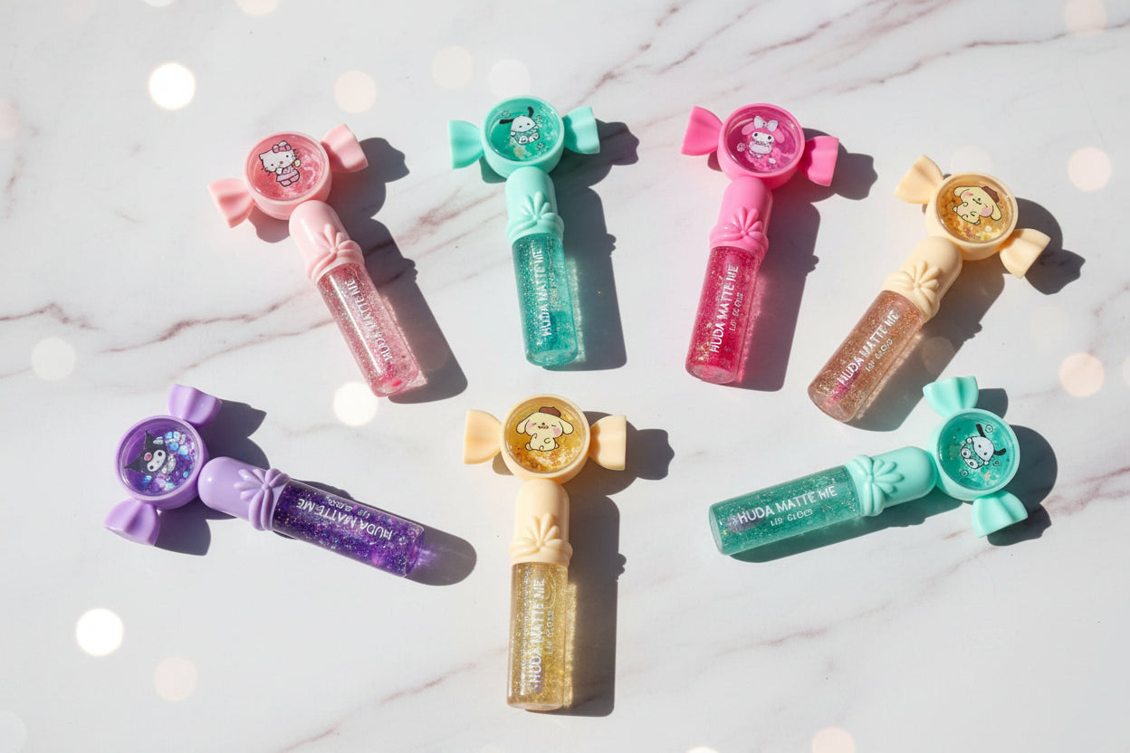 Six small lip gloss tubes with bow-shaped caps and round character medallions, arranged on a white faux-fur surface. The tubes come in pink, mint green, purple, peach, and light blue, with glittery translucent bodies and Hello Kitty branding visible on the packaging.