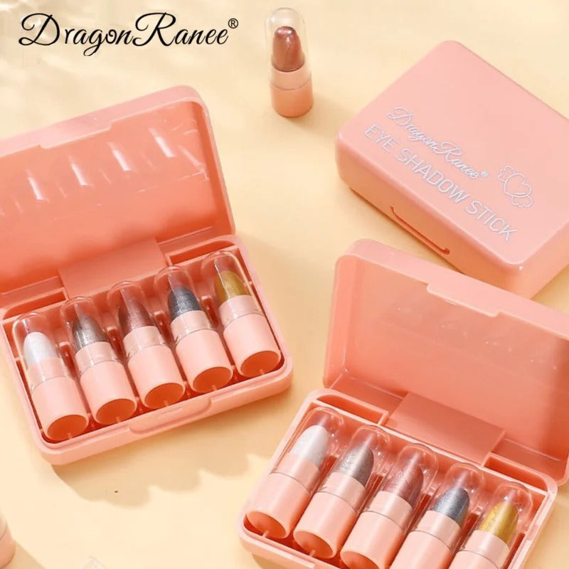 DragonRanee makeup shadow stick set in pink plastic cases, shown open with multiple lipstick-style sticks inside, arranged on a warm cream background with a few loose sticks nearby.