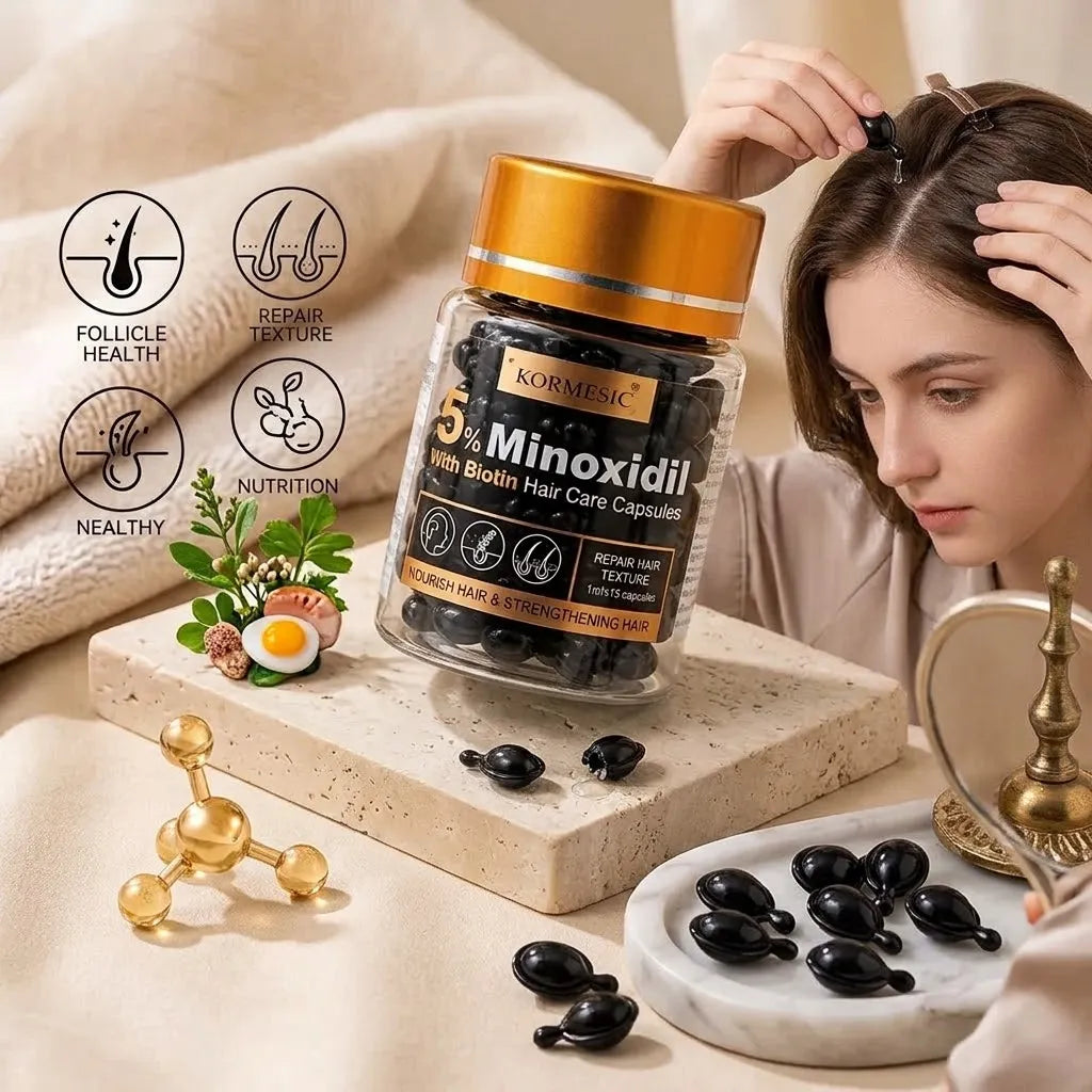 A bottle of Kormesic 5% Minoxidil hair growth capsules is displayed on a beige fabric surface next to a woman looking into a mirror. The bottle has a gold cap and a black label with gold text, and several black capsules are scattered around it.