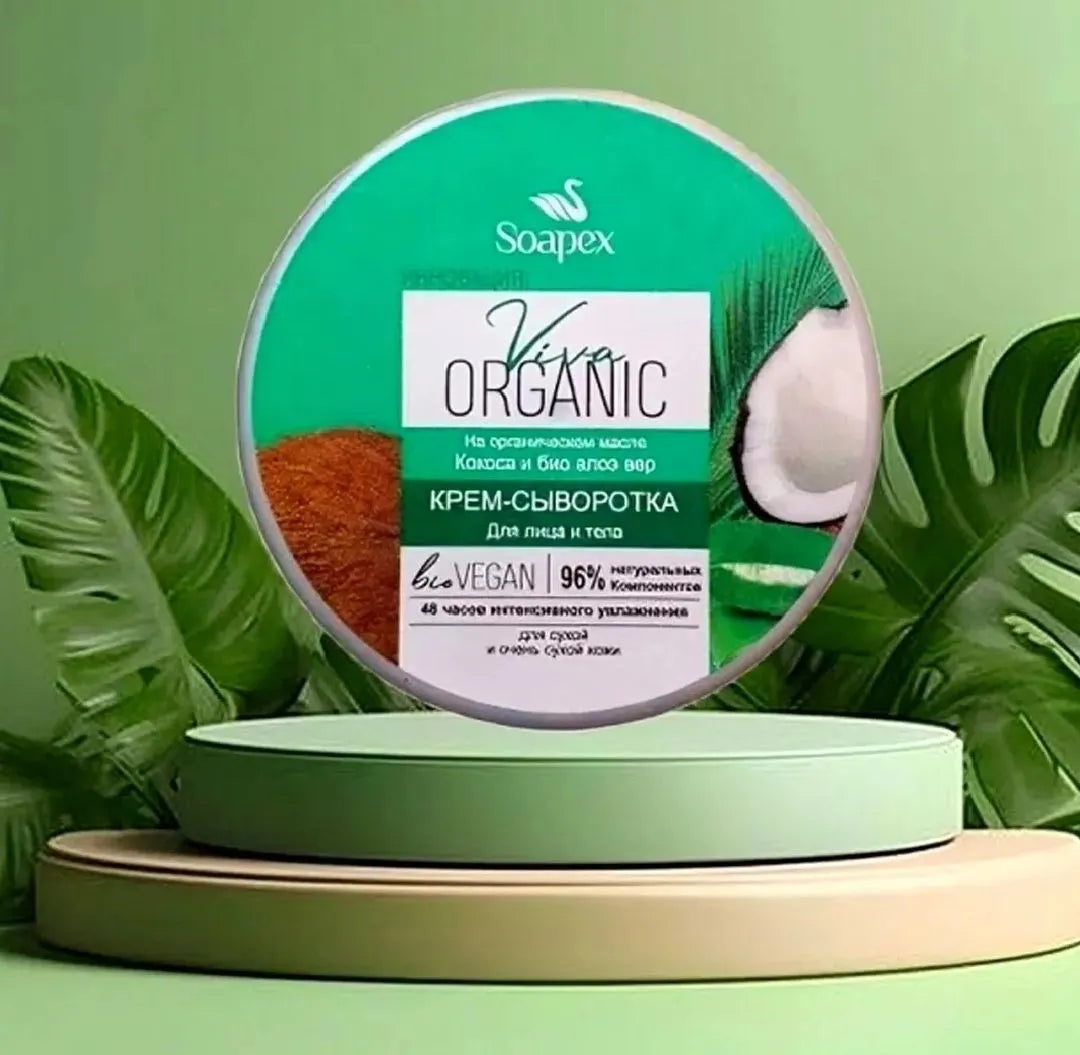 A round container of Soapex Organic cream soap displayed on a two-tiered light green and beige pedestal, surrounded by green tropical leaves against a light green background.