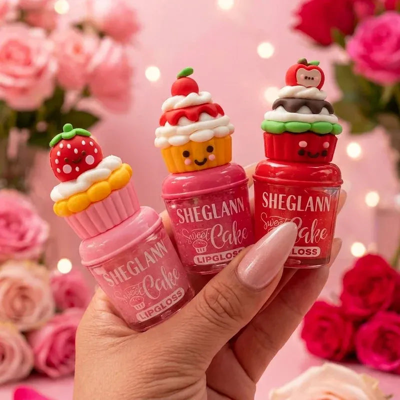 Three small lip gloss bottles shaped like cupcakes are held in a hand against a pink floral background. The bottles are labeled SHEGLANN Sweet Cake Lipgloss Loss, with cupcake tops in strawberry, vanilla, and chocolate flavors.
