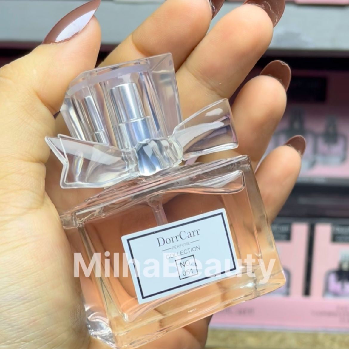 Hand holding a clear perfume bottle with a visible label, brand 'Dorrcarr' on a blurred background.