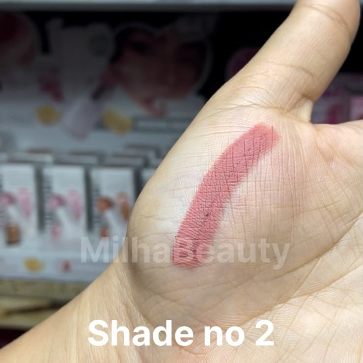 A close-up of a hand showing a swatch of mauve-pink makeup shade on the back of the palm, with overlaid text reading 'Shade no 2' and a phone app interface around it.