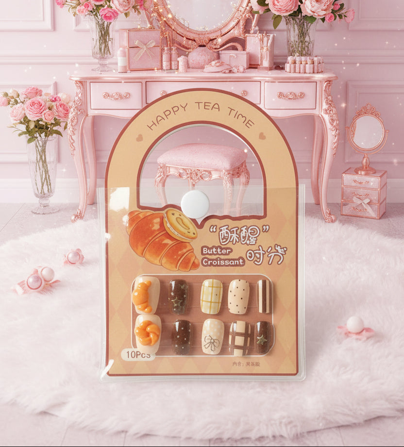 A 10-piece set of false press-on nails in a peach-colored 'Happy Tea Time Croissant' themed package, resting on a black laptop keyboard.