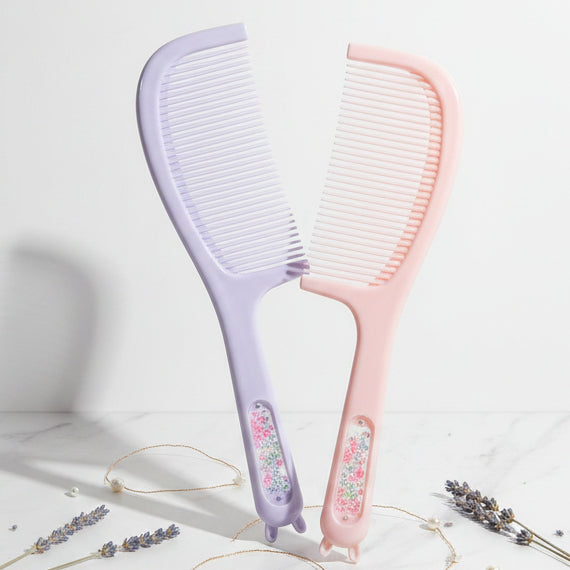 Two packaged hair care combs on a patterned fabric background. The left comb is lavender with a glittery pink handle, and the right comb is pastel pink with a glittery multicolor handle.