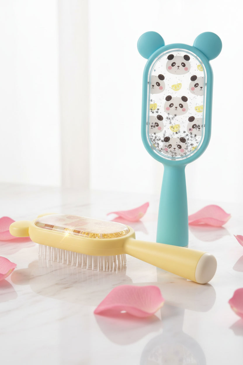 Two packaged hair brushes displayed side by side in clear plastic retail boxes. The left brush is pale yellow with a bear-face cutout and pink bear illustrations inside, with gold glitter visible.