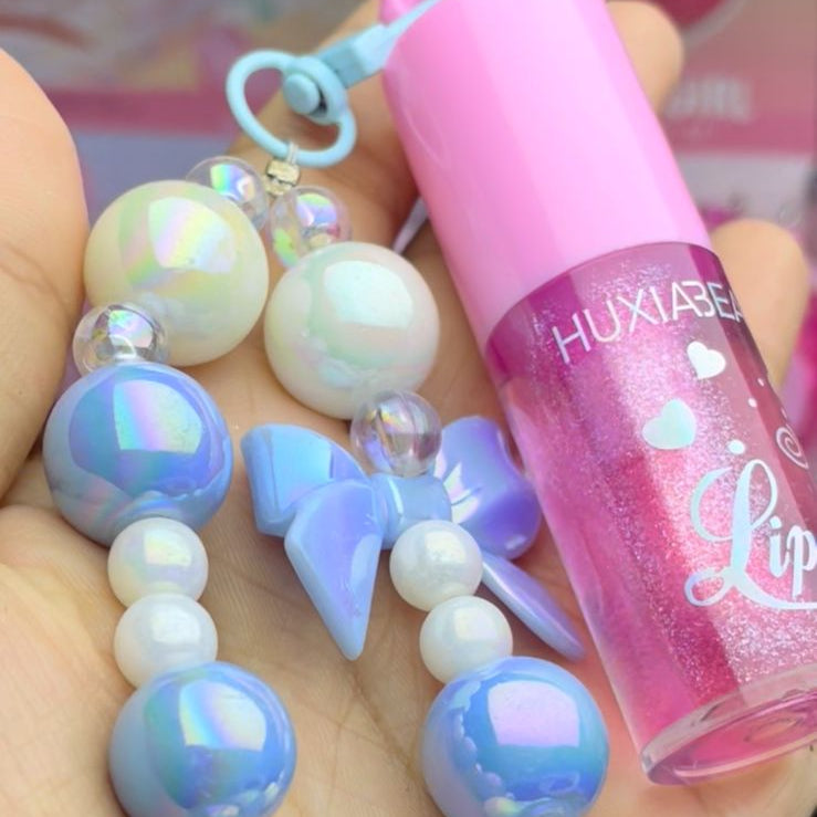 Hand holding a colorful beaded necklace and pink lip gloss with 'HUXIA BEAUTY' branding.