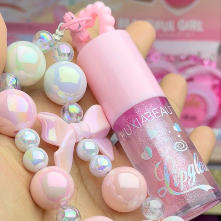 Pink lip gloss with decorative beads held in a hand
