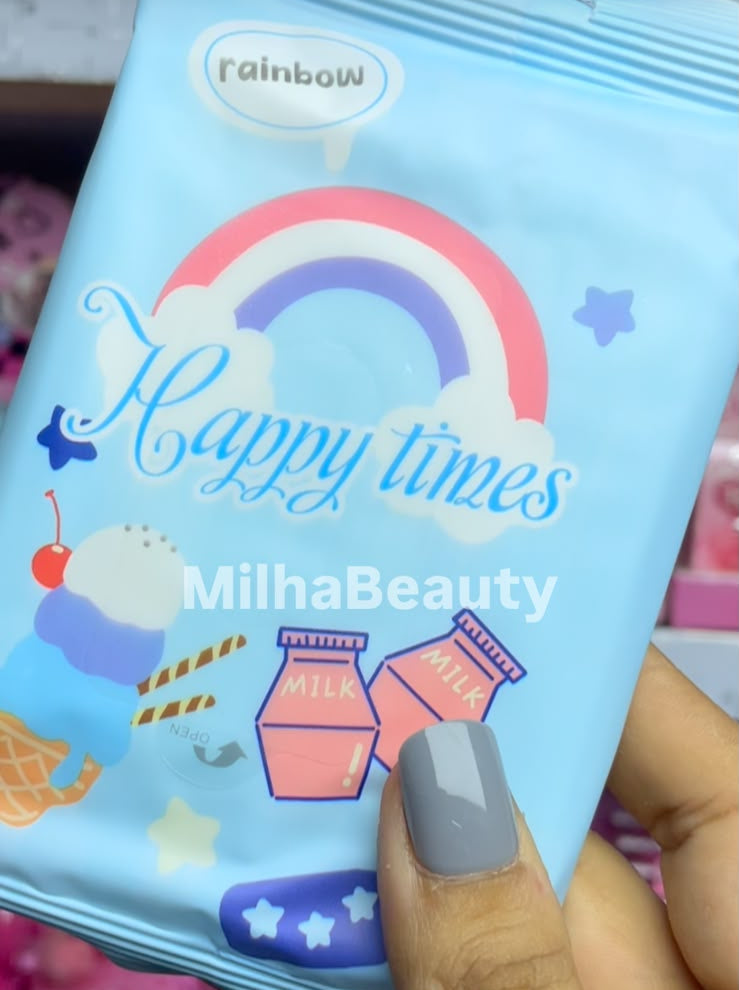 A hand holding a light blue packet of Rainbow Happy Times MilhaBeauty lip gloss, with a rainbow and pink gloss bottle illustration on the front.