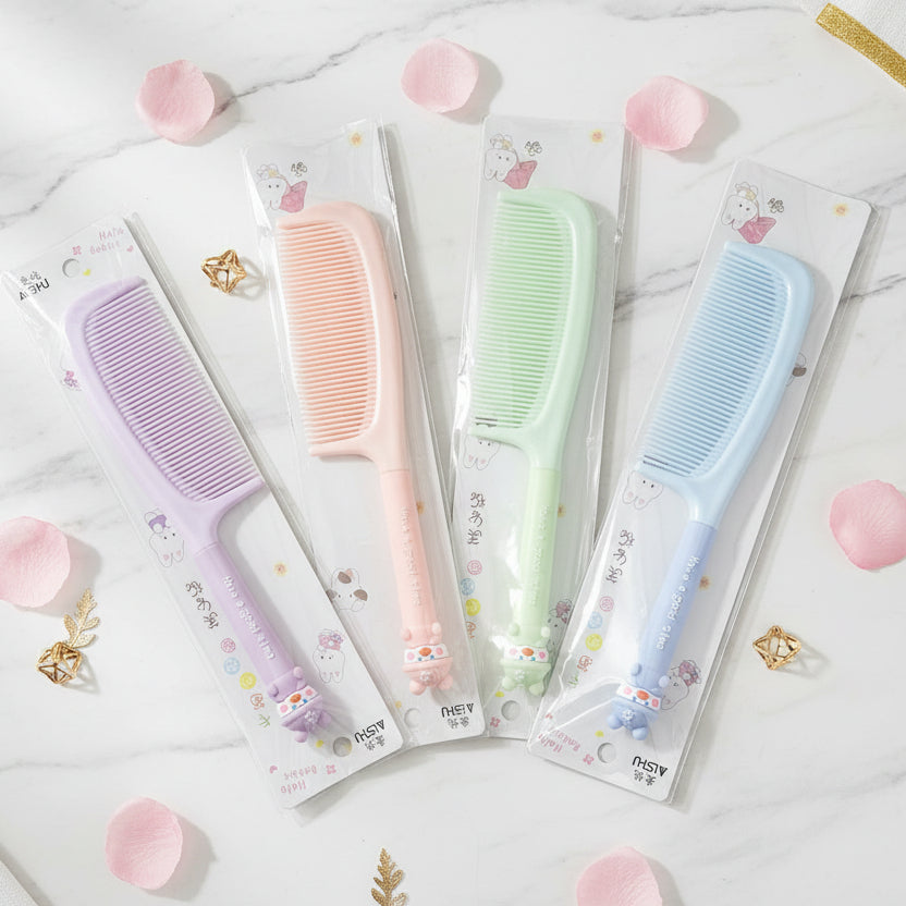 Three packaged plastic hair combs in pastel colors are laid out on a patterned fabric surface. The combs are purple, pink, and light green, each in its own retail blister pack with a cartoon cat decoration at the end of the handle.