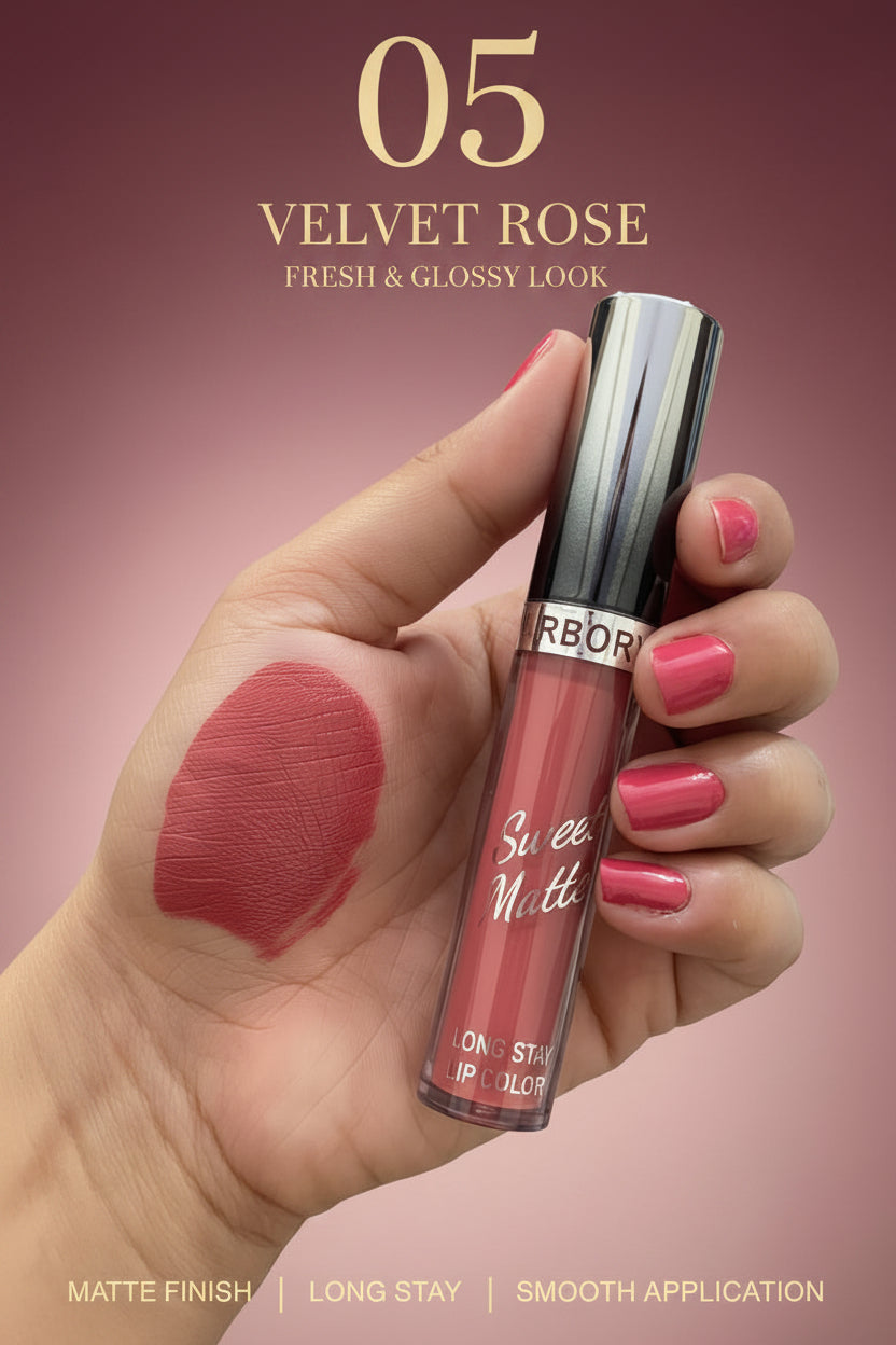 A hand holding a tube of Roraba Sweet Matte liquid lipstick, with a swatch of the deep berry-red lipstick color applied on the back of the hand. Other lipsticks are visible in the background.
