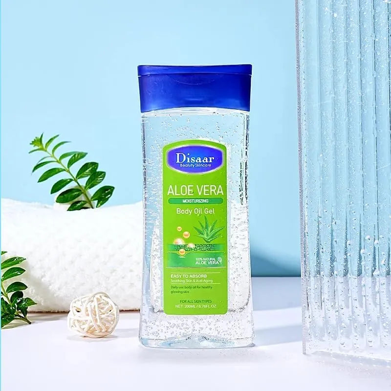 A bottle of Disaar Aloe Vera Moisturizing Body Oil Gel, featuring a blue cap and green label, styled on a white surface with a white towel, green leaves, and a textured glass prop against a light blue background.