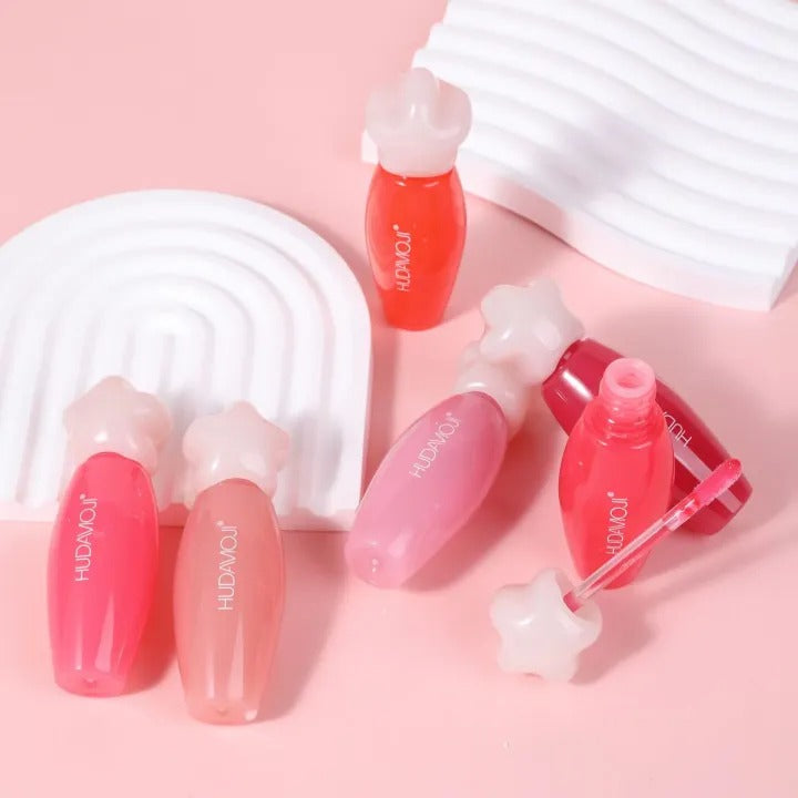 Set of red and pink lip glosses with visible brand name on a pink background HUDAMOJI