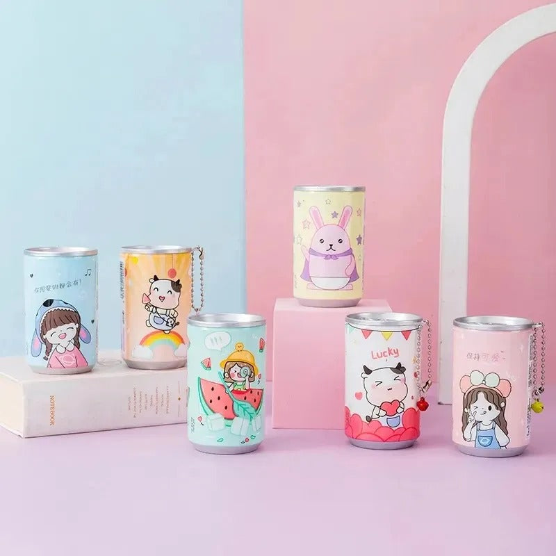 Five colorful metal beverage cans with cute cartoon illustrations are arranged on pink and light blue display blocks against a pastel pink and blue studio background. The cans feature characters like a bunny, a girl with a bow, and a child with watermelon slices, and each can has a small hanging charm.