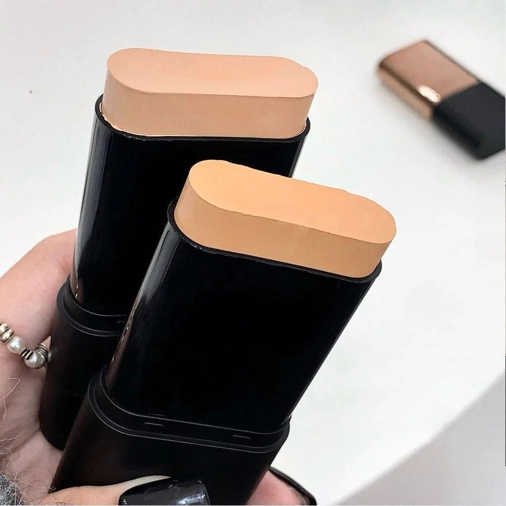 Two black makeup sticks with beige caps held by a hand on a white background