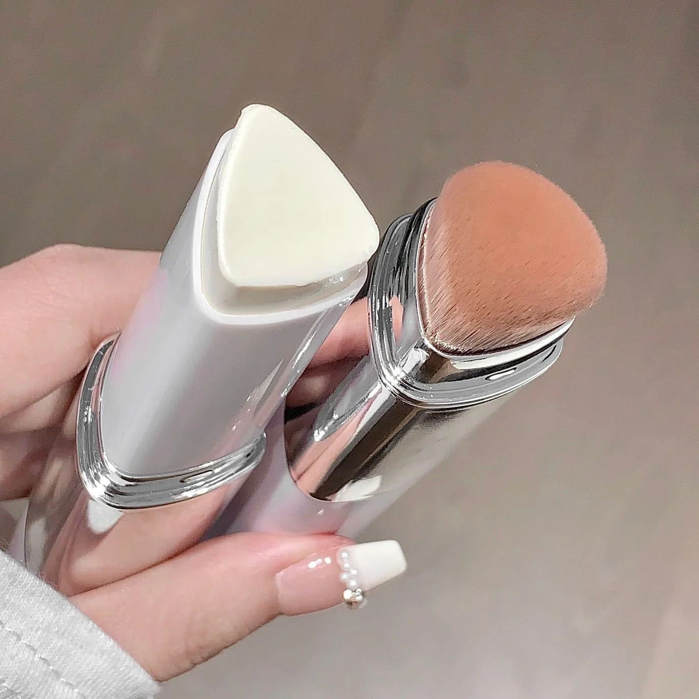 kakashow stick foundation Hand holding a cosmetic stick with a brush attachment against a neutral background