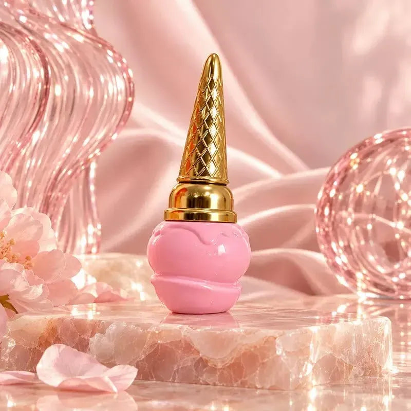 A pink cosmetic bottle with a sculpted, rounded base and a tall, textured gold cap, styled on a polished stone slab with pink fabric, decorative glass spheres, and soft petals.