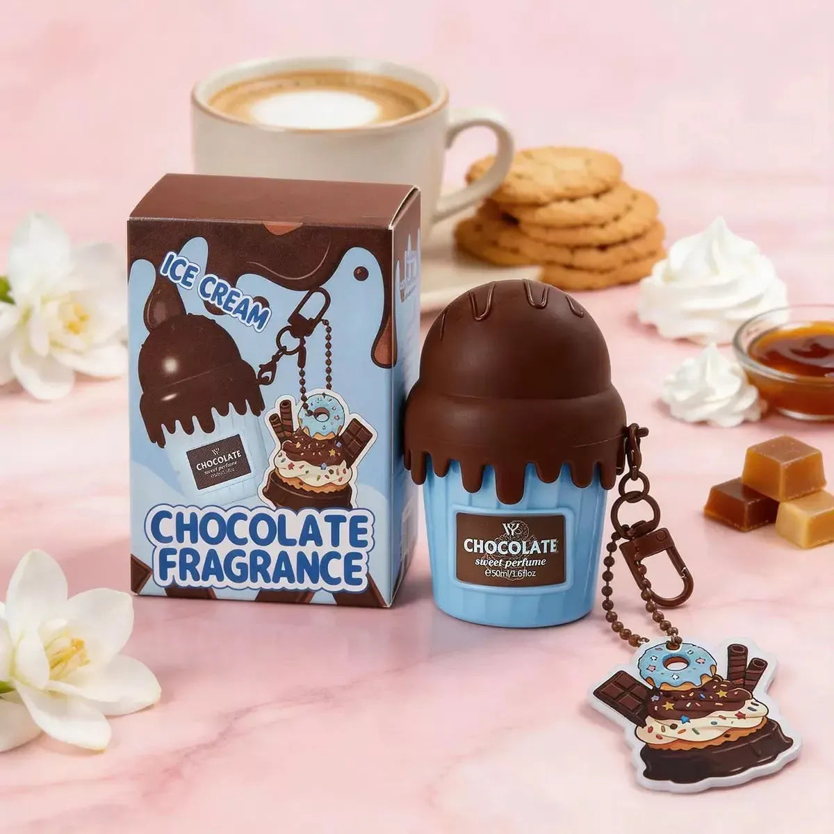 Chocolate-themed perfume bottle with packaging and keychain on a pink background with cookies and flowers.