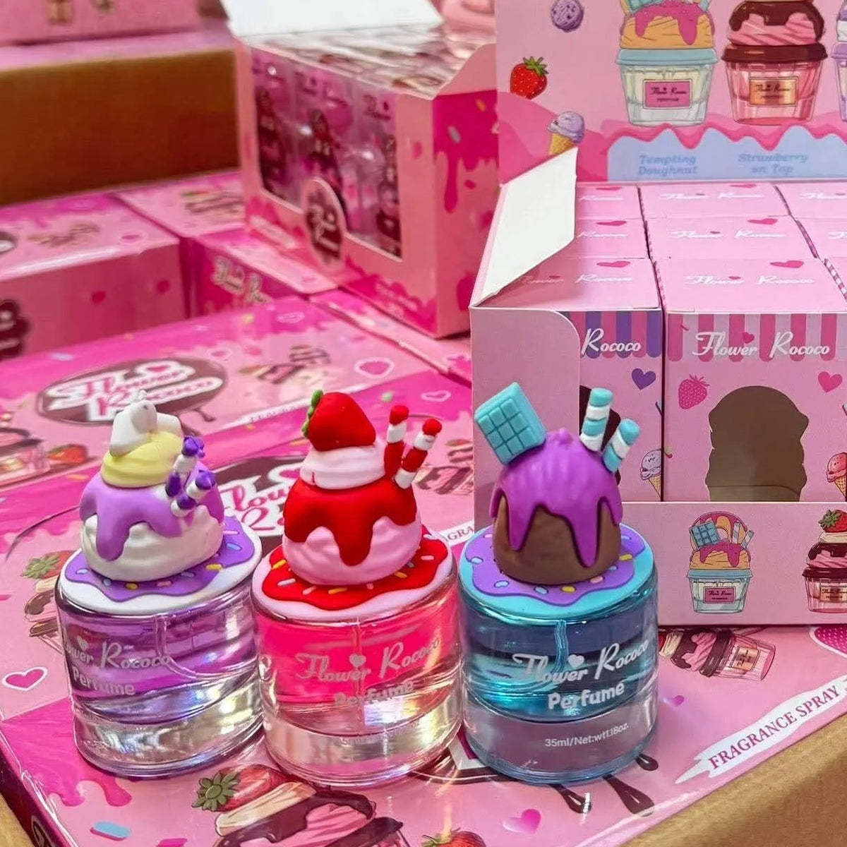 A pink display box filled with small blind-box packages and several colorful toy figures topped with dessert illustrations, photographed in a retail store setting with shelves of similar products in the background.