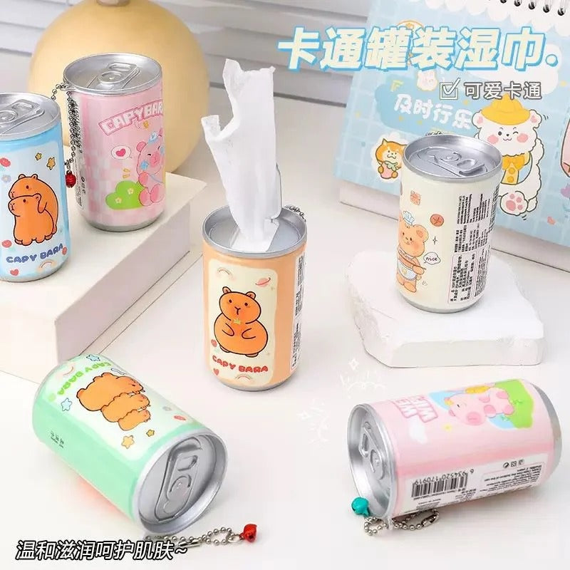 A set of novelty tissue boxes shaped like cartoon canned drinks, each with a pull-out tissue and a small keychain charm, shown on a white tabletop with decorative blocks and a book in the background.