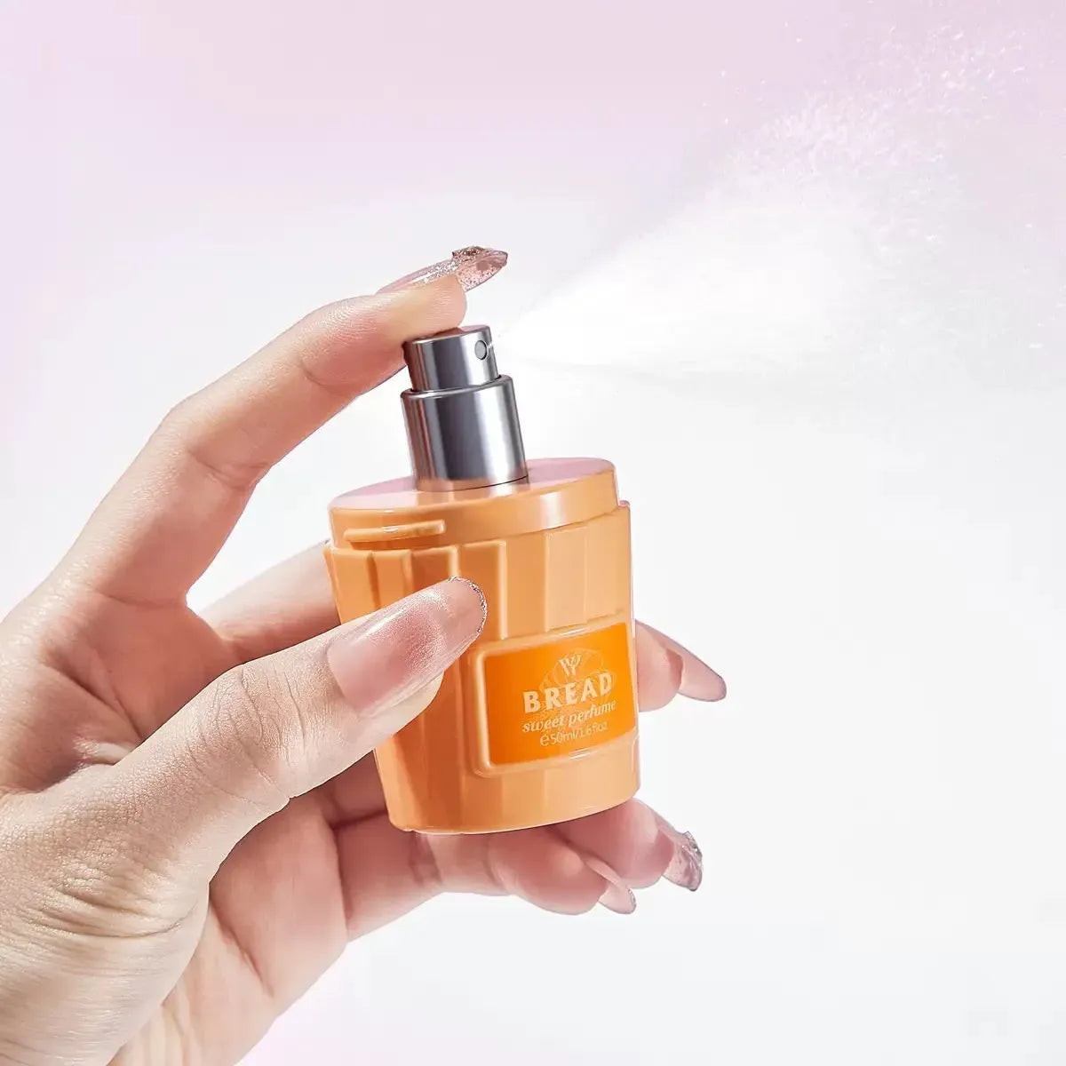 Hand holding an orange perfume bottle with a silver cap on a light pink background