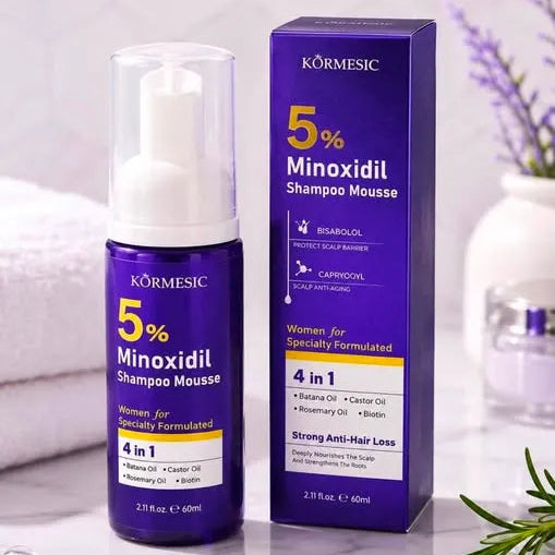 Körmesic 5% Minoxidil Shampoo Mousse bottle and its matching purple packaging box, displayed on a light marble surface with spa-style props like a towel, lavender, and rosemary.