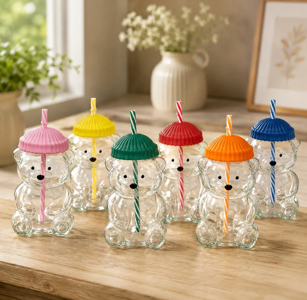 Set of clear bear-shaped cups with colorful lids and straws on a wooden surface.