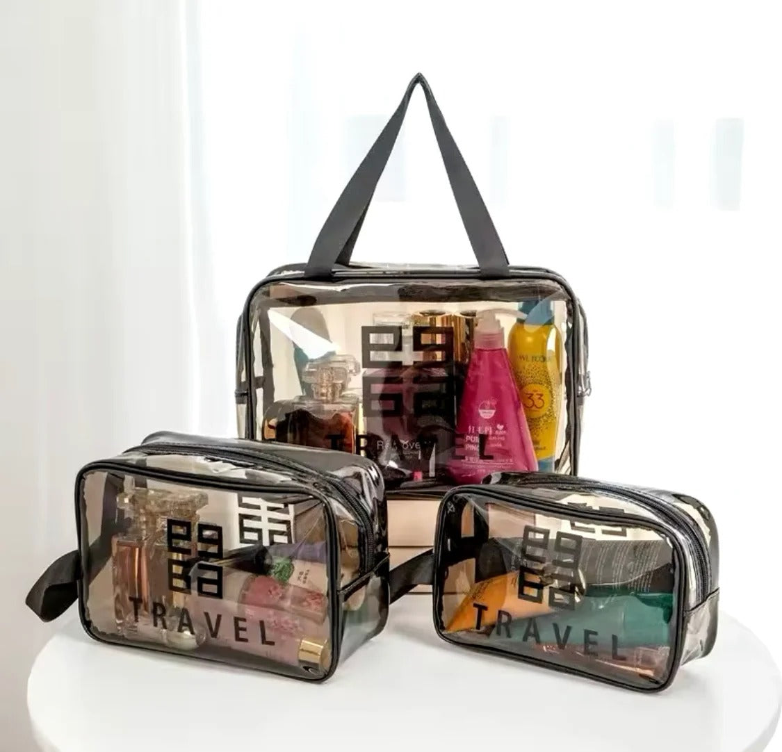 Three clear plastic travel toiletry bags with black handles and black printed geometric logos, shown on a white round table against a bright white background.