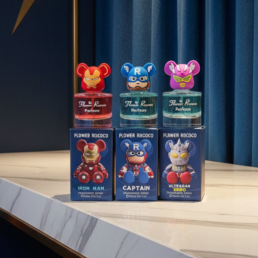 Three small perfume bottles with colorful character caps and matching blue boxes are shown against a comic-style red and blue background. The bottles appear labeled 'Flower Ro Coco' and feature Marvel-inspired characters: Iron Man, Captain America, and Ultraman