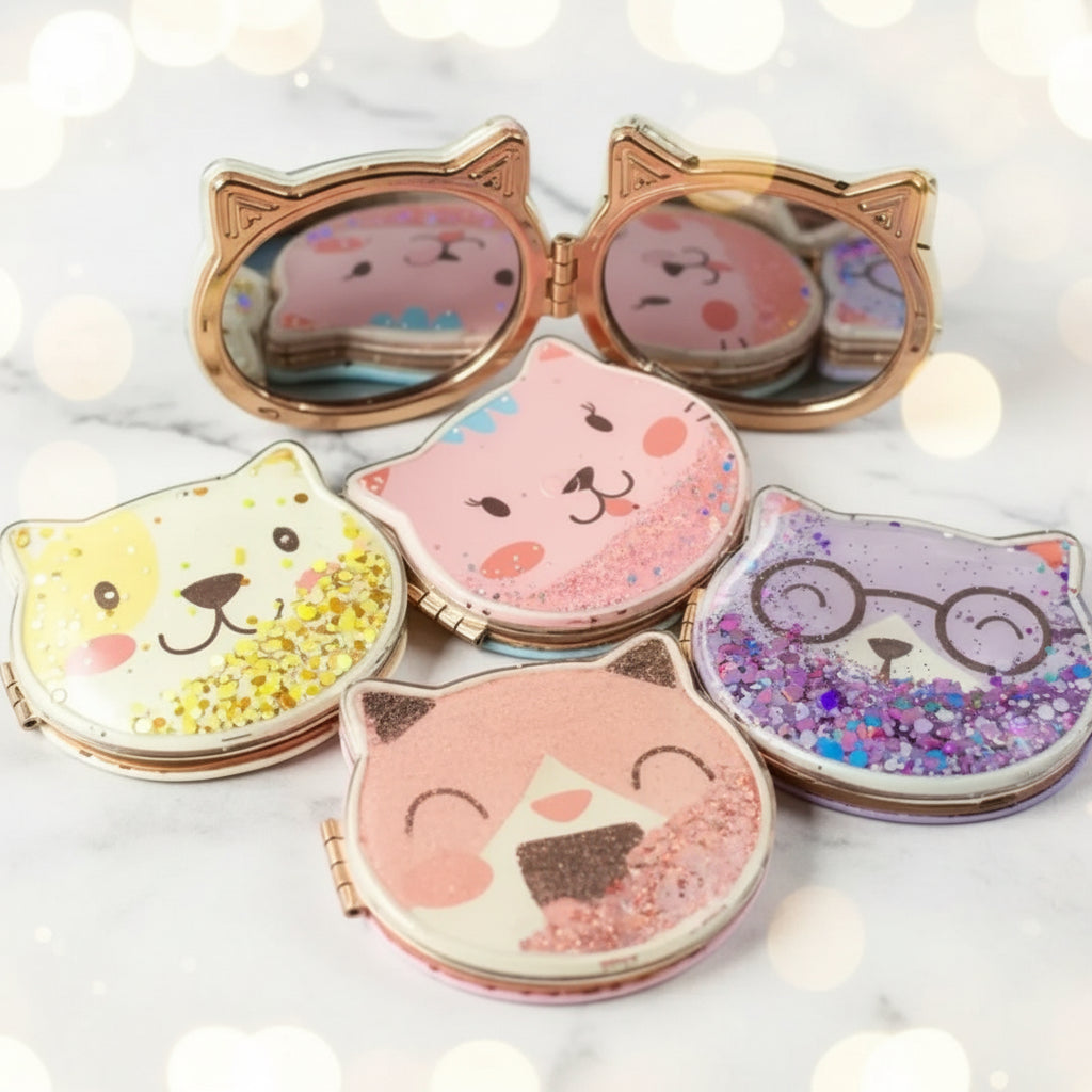Four cat-face compact mirrors with gold-tone frames, arranged on a white background. Each compact has a different cat design with glitter accents: yellow, pink, purple, and brown.