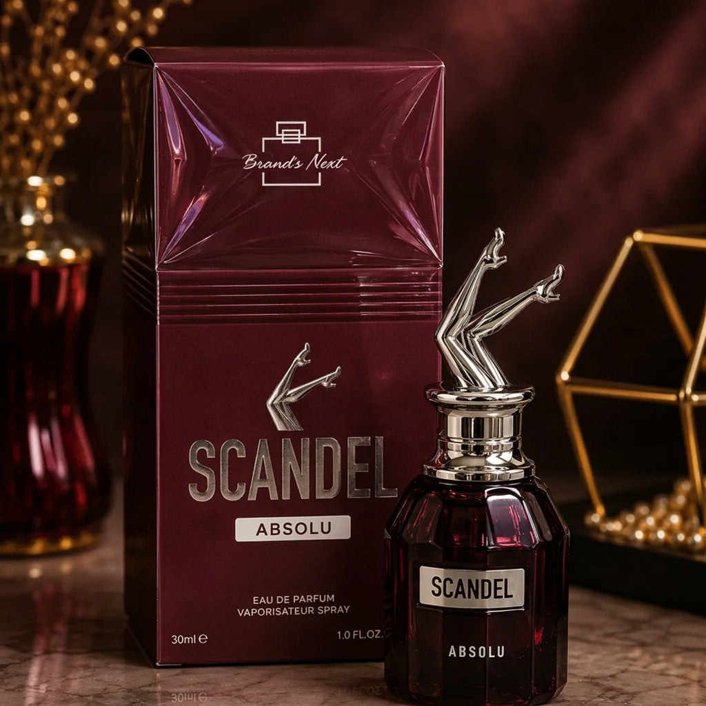 A bottle of Brand's Nectar Scandal Absolu Eau de Parfum next to its matching box, both in a deep burgundy color with silver accents, set against a dark, warm, and atmospheric background with bokeh lights.