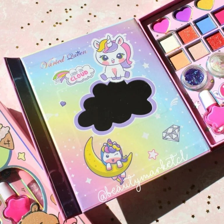 A pastel multicolor makeup palette set featuring cartoon unicorn illustrations on the packaging, shown open with eyeshadow pans, a glitter jar, and pink cosmetic items inside. The set is photographed on a pink glittery surface.