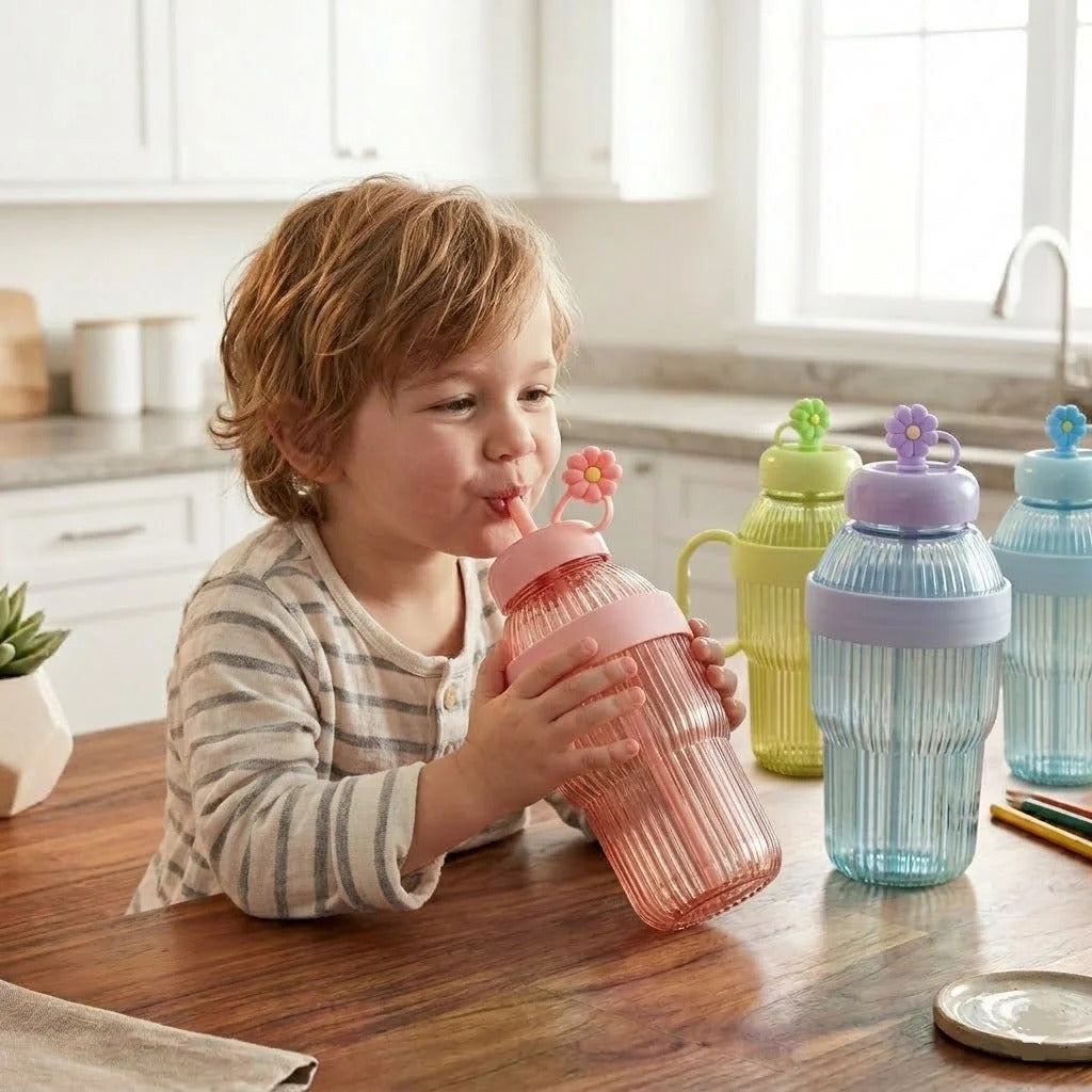 Child drinking from a pink sippy cup with colorful water bottles on a kitchen counter.