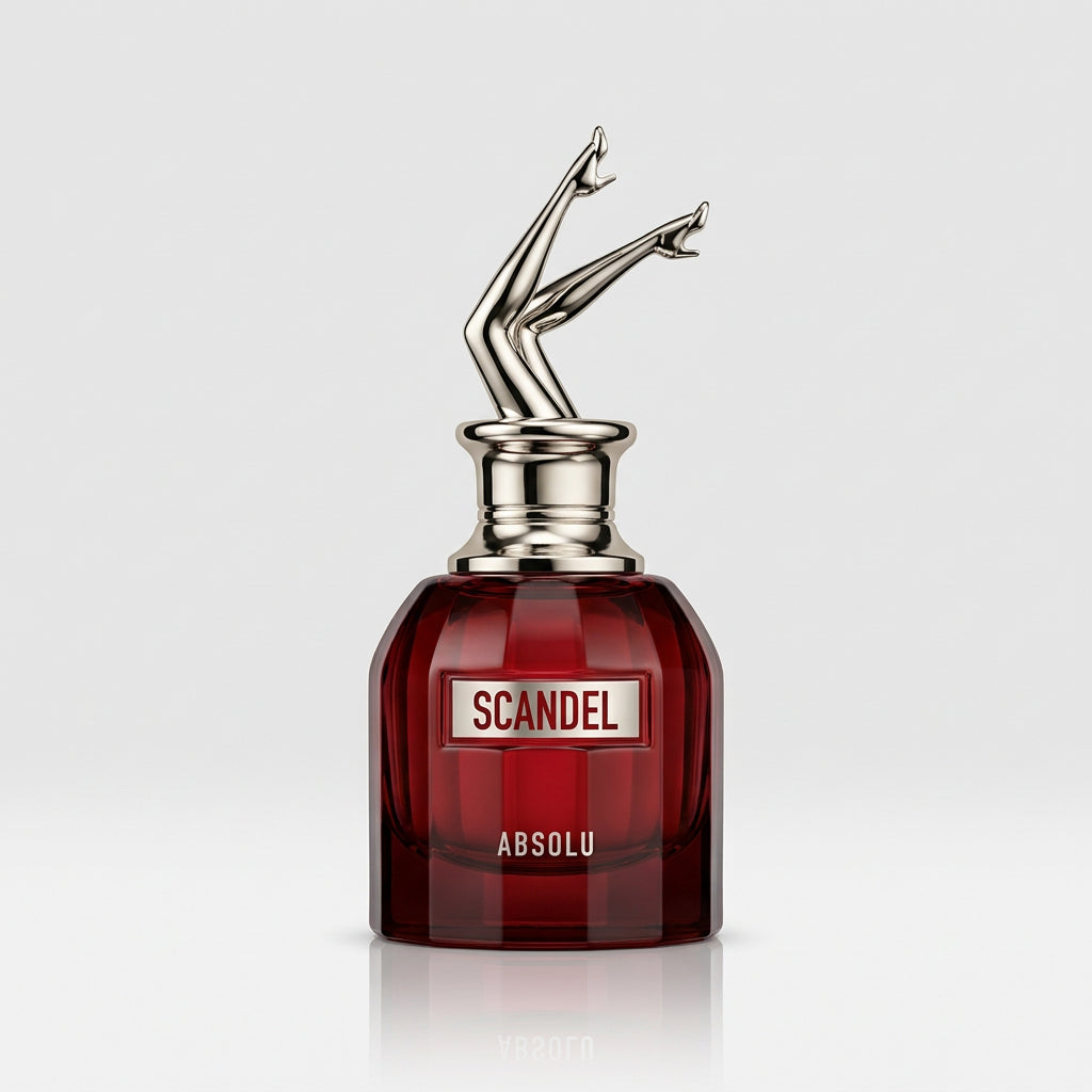 A hand holding a small dark amber glass perfume bottle with a silver metal atomizer cap shaped like a stylized figure. The bottle label reads 'SCANDEL ABSOLU'.