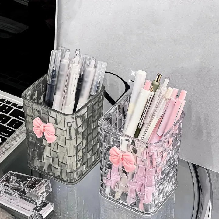 Two clear pen holders with pink bows on a desk.