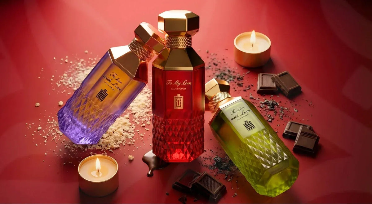 Three luxury perfume bottles with gold caps arranged on a red surface with candles, chocolate pieces, and scattered powder. The bottles contain purple, red, and green liquids with gold labels.