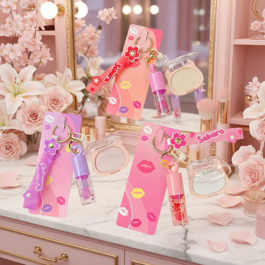 Four pink and purple cosmetic keychains with matching card holders, lip gloss tubes, and compact powder cases arranged on a black textured background.