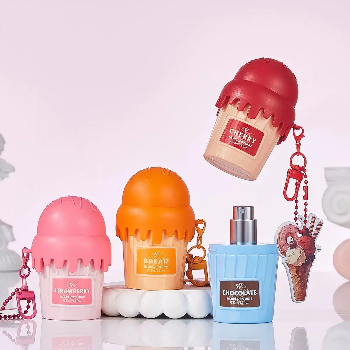 Four novelty lip balm containers shaped like ice cream cones in pink, orange, and blue, alongside a chocolate-themed keychain, displayed on a reflective white surface against a soft pink background.