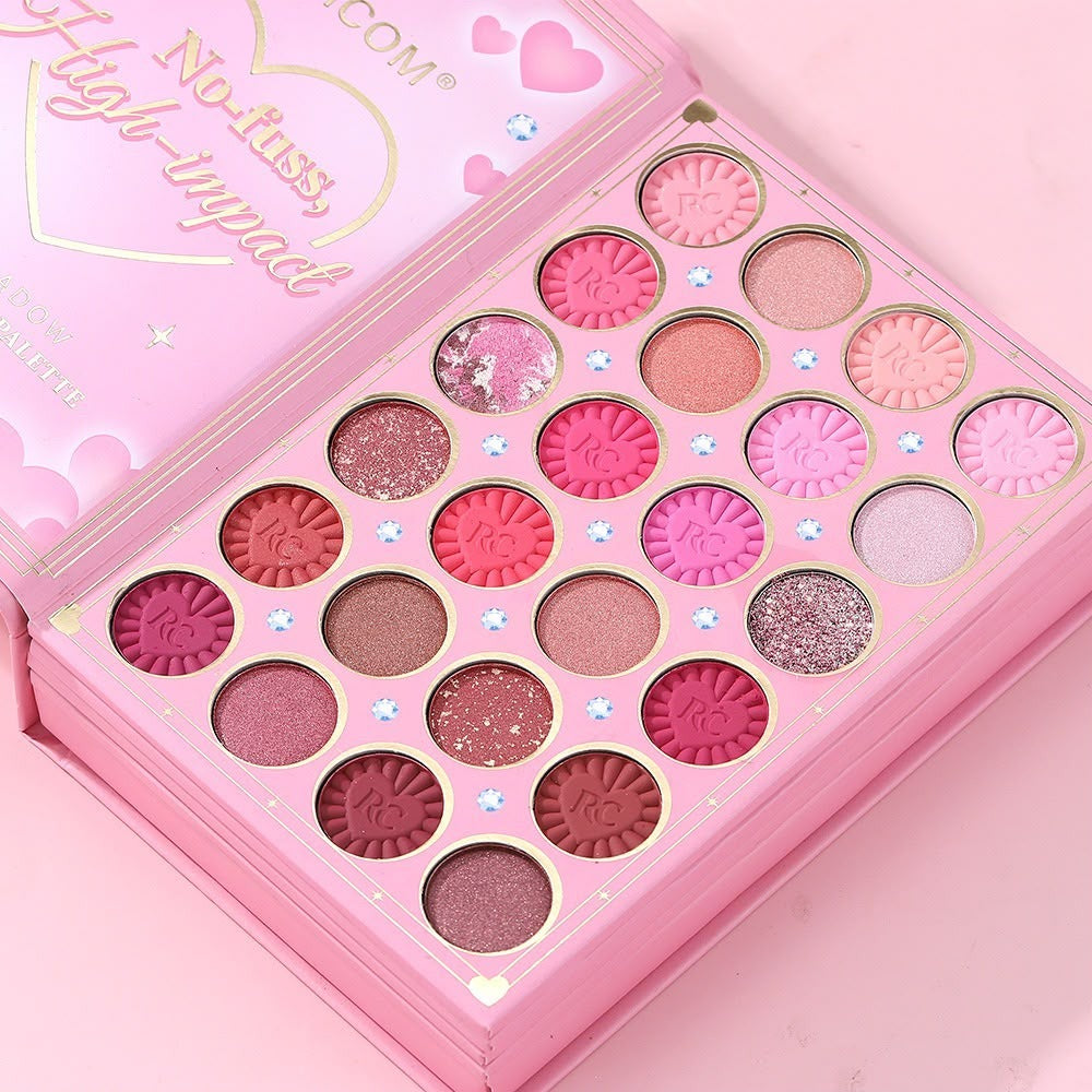 A pink makeup palette with 24 eyeshadow pans in various shades of pink, red, rose gold, and glitter, shown open on a matching pink background.
