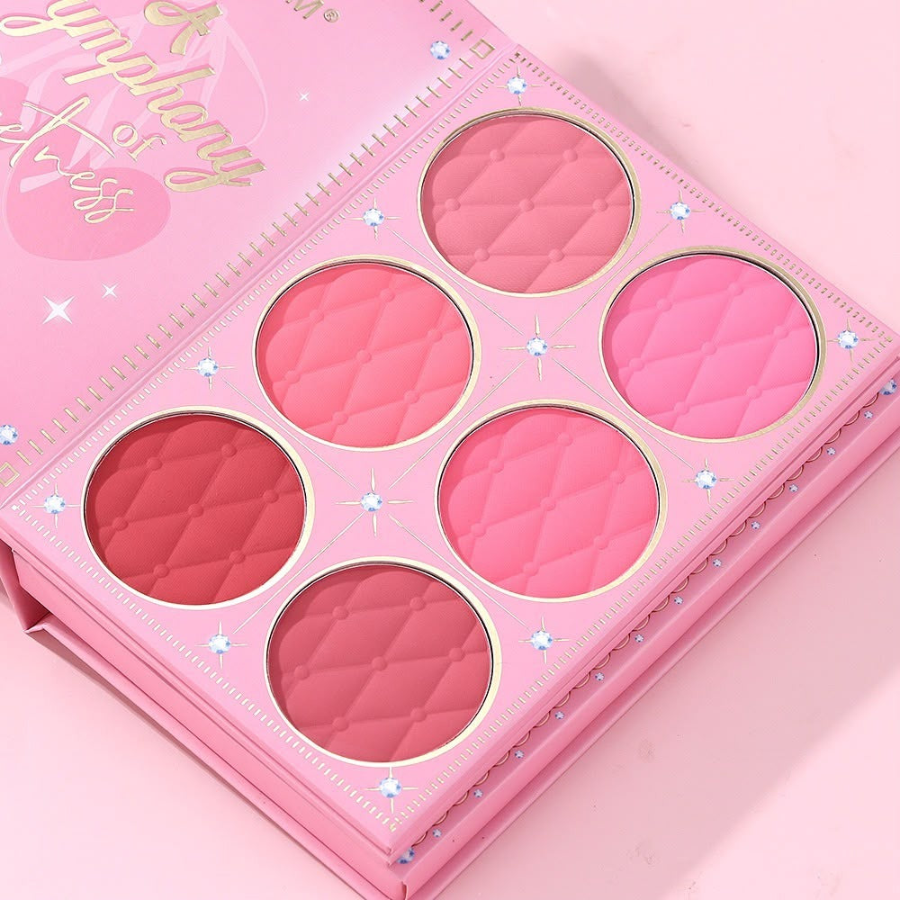 A pink makeup palette with six quilted circular pans in shades of pink, coral, and berry, shown open on a matching pink background. The palette cover reads 'Symphony of Stress' in gold script.