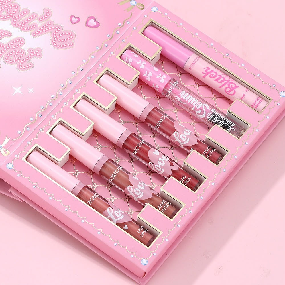 A pink makeup gift set in a decorative box, containing six lip gloss tubes in shades of pink, nude, and brown, with a matching lip gloss pen placed on top.