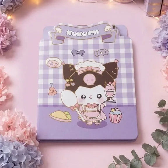 A pastel pink desk setup featuring a cute character clipboard with a lavender and white gingham pattern and a cartoon character holding a spoon and cupcake. The desk is decorated with pink and blue hydrangeas, eucalyptus leaves, a pencil cup, and washi tape.