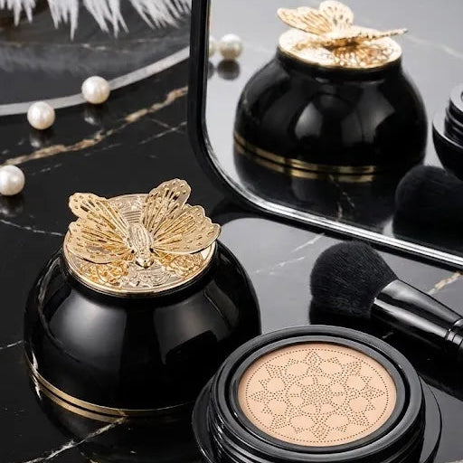 Jar beside makeup brush: “Gegemoon cushion foundation with gold butterfly lid beside an open foundation cushion and makeup brush”