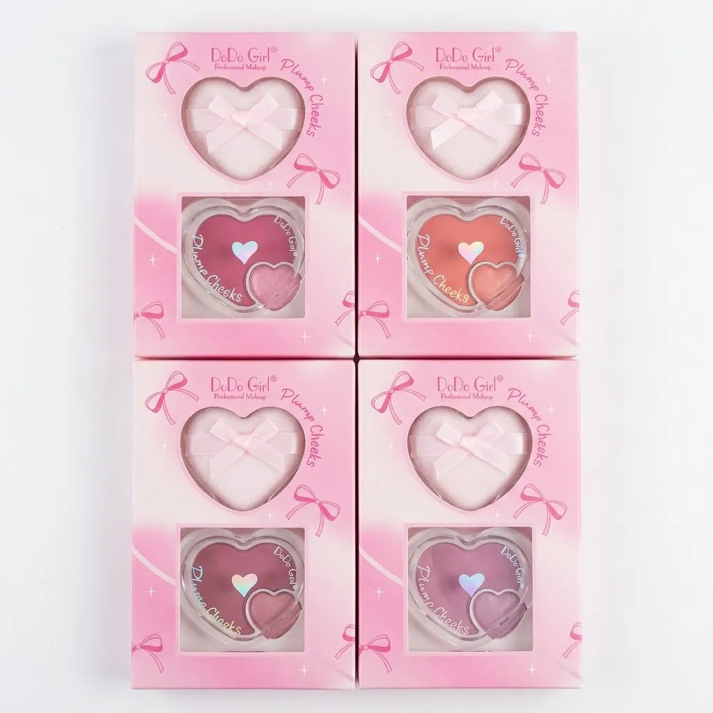 Four pink heart-shaped cosmetic compacts arranged in a 2x2 grid on a white background. Each compact has a heart-shaped window showing a different blush shade: pale pink, light pink, coral pink, and mauve pink.