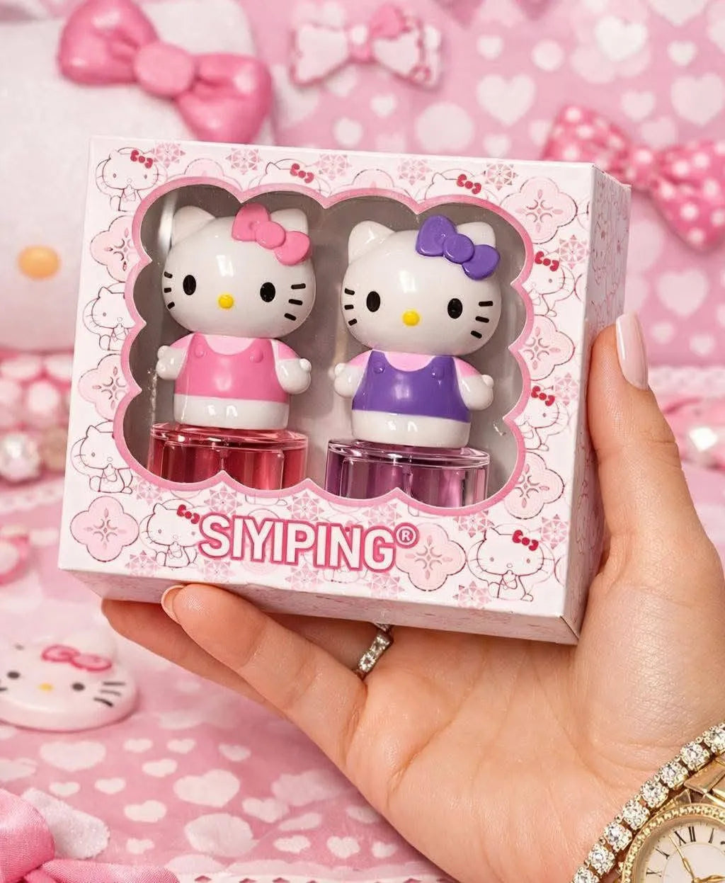 A hand holds a pink Hello Kitty themed SIMPING gift box containing two small character-shaped items, one in pink and one in purple, against a pink heart-patterned background.